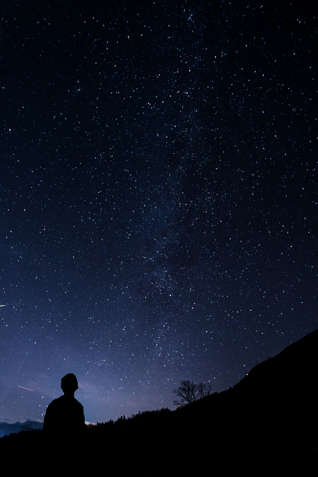 A lone figure silhouetted beneath a vast star-filled night sky