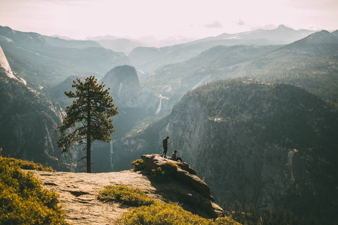 Two people standing on a cliff edge overlooking a vast misty mountain valley