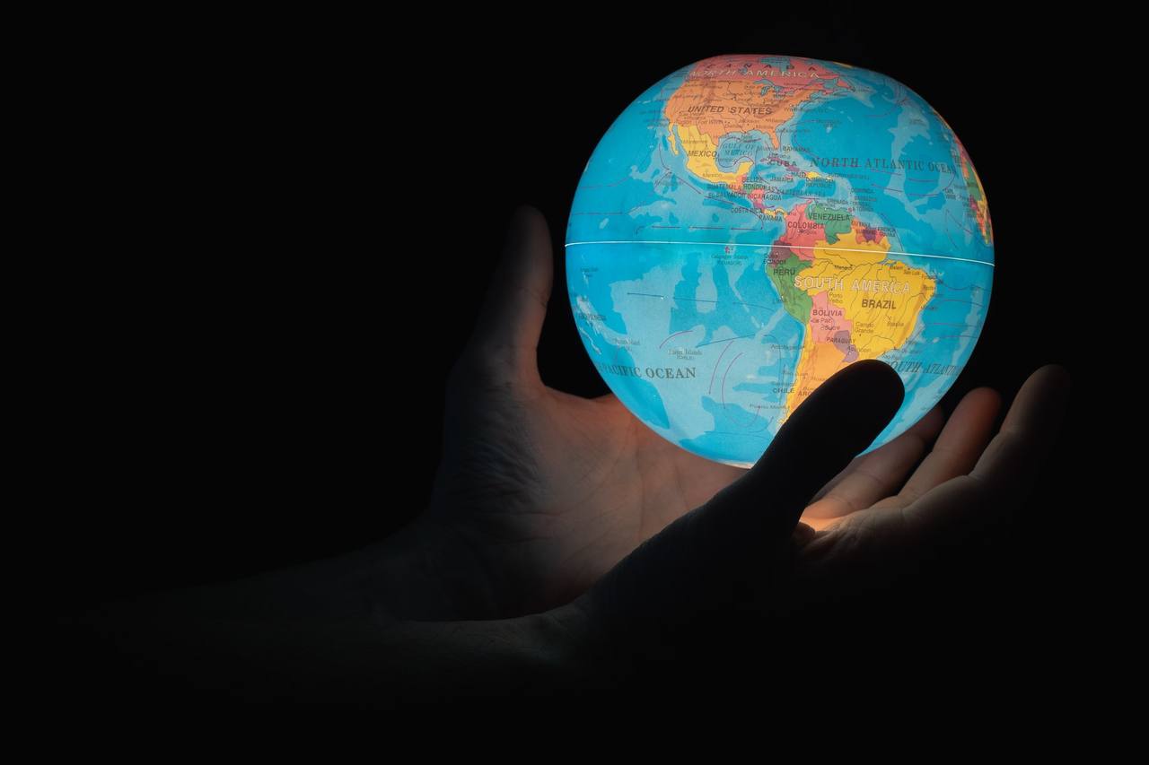 A hand cupping a small glowing globe of the Earth against a dark background