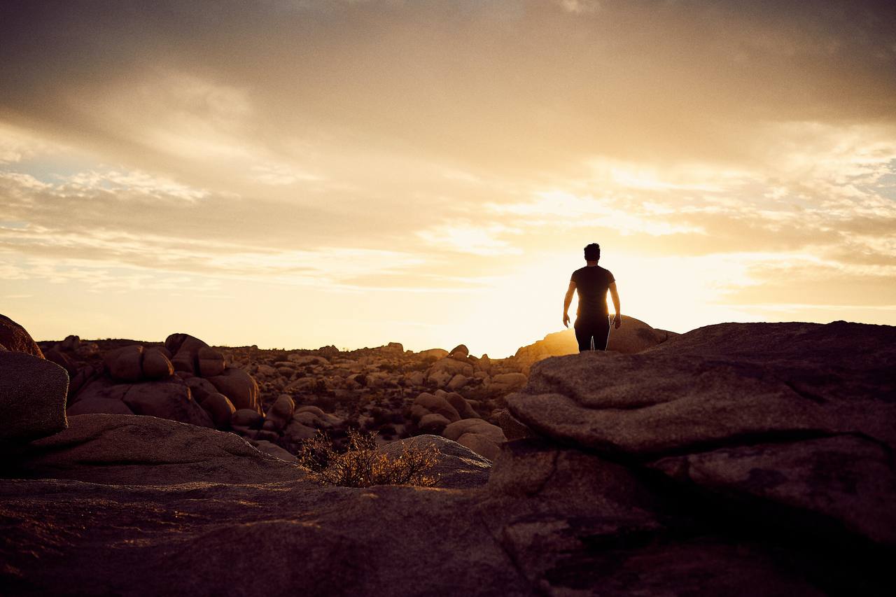 A lone figure walking toward the sunrise across a field of boulders
